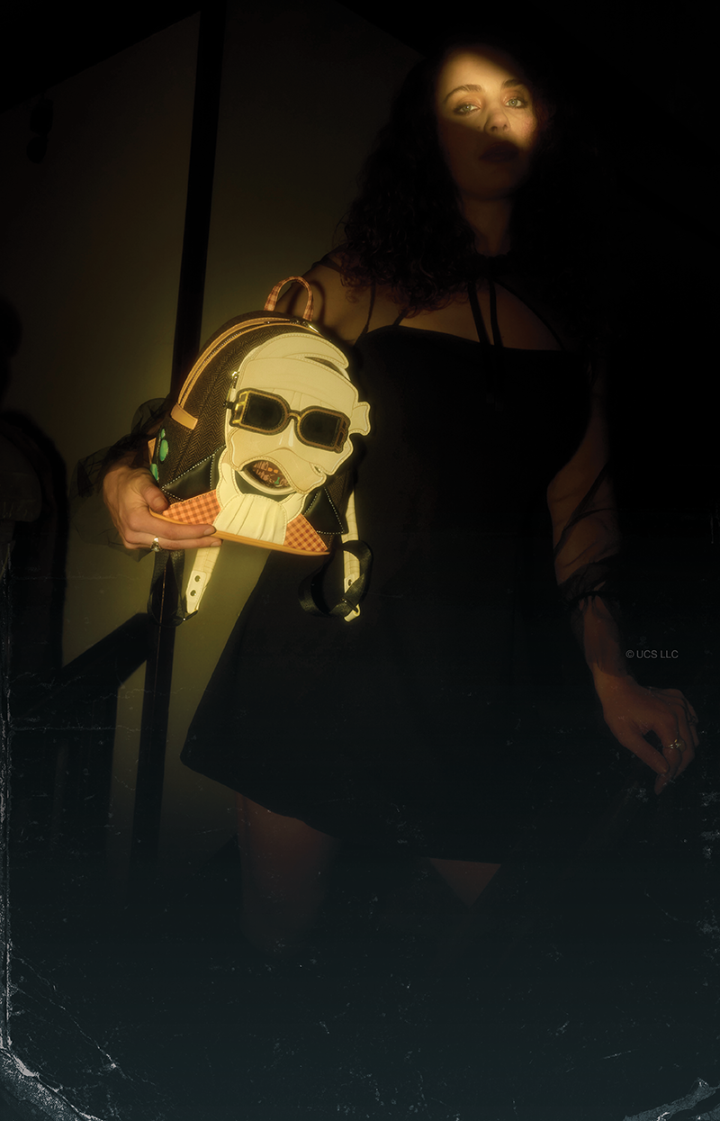 Dark spooky background with glowing Yellow shutter light on models eyes holding Loungefly Universal Monsters Invisible Man Cosplay mini backpack