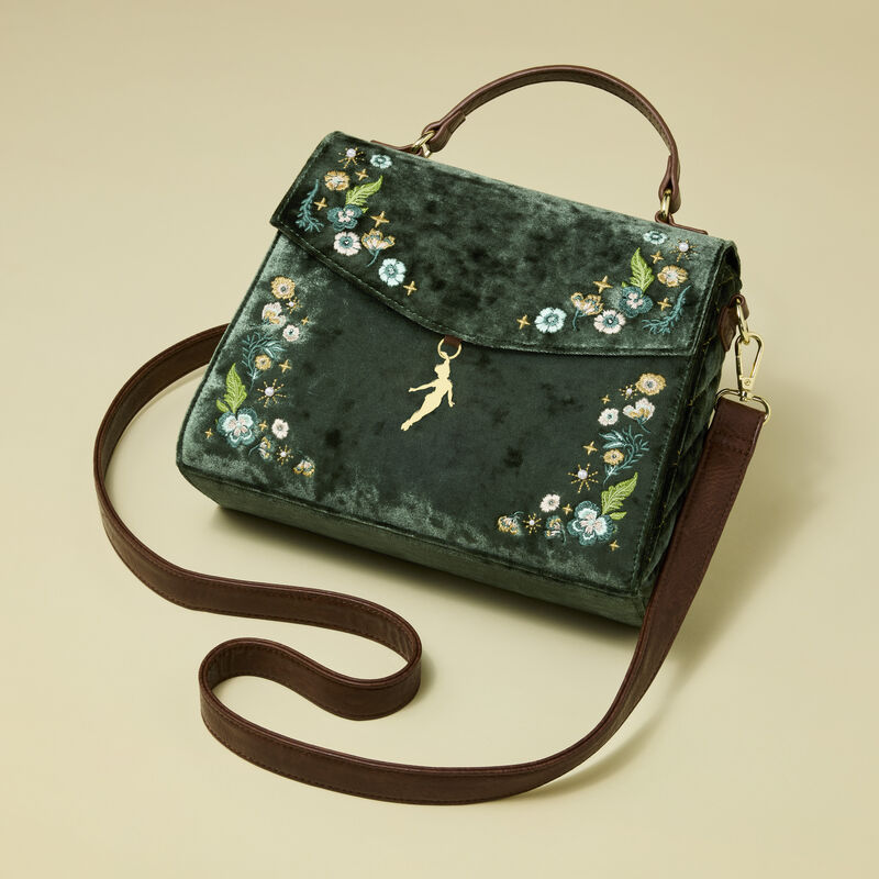 Woman looking past camera, wearing an olive green blouse and blue jeans, posing with the Loungefly Peter Pan Quilted Texture Crossbody Bag. She stands against a light green background. 