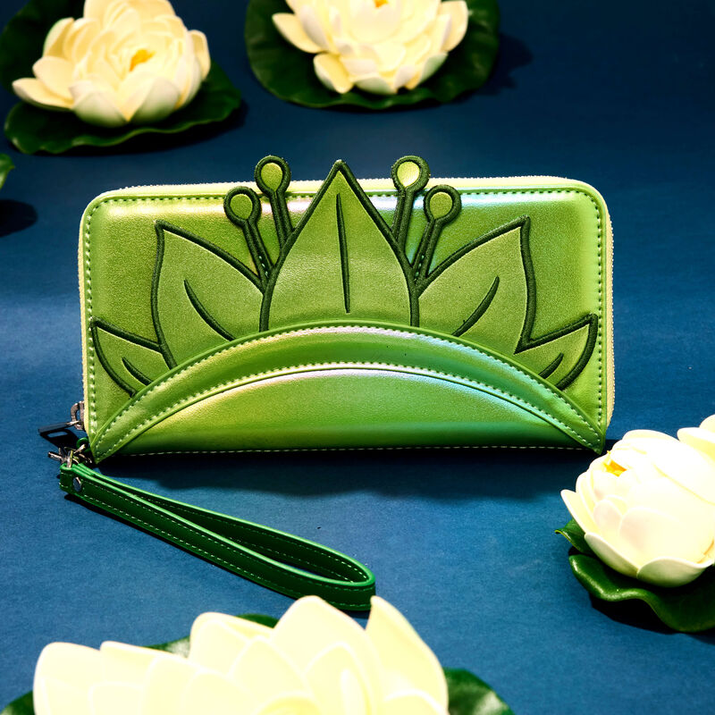 Iridescent green zip around wallet with an appliqué of Princess Tiana's crown. The wallet sits against a blue background surrounded by white water lilies. 