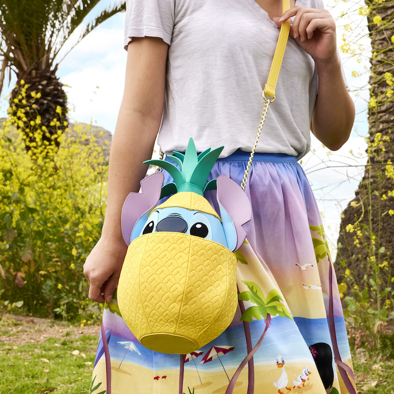 Woman outside wearing a white top with a beach-themed Lilo and Stitch skirt, modeling the Stitch Shoppe Pineapple Stitch Crossbody Bag