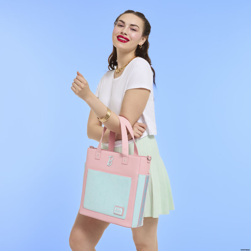 Woman smiling at camera wearing a white top and green skirt. She holds the Loungefly Classic Barbie tote bag over one arm. She stands against a blue background. 