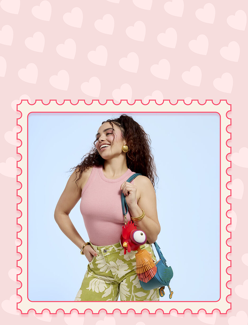 Blue background with model showcasing Loungefly Moana Hei Hei Crossbody bag with pink heart background and postcard stamp border