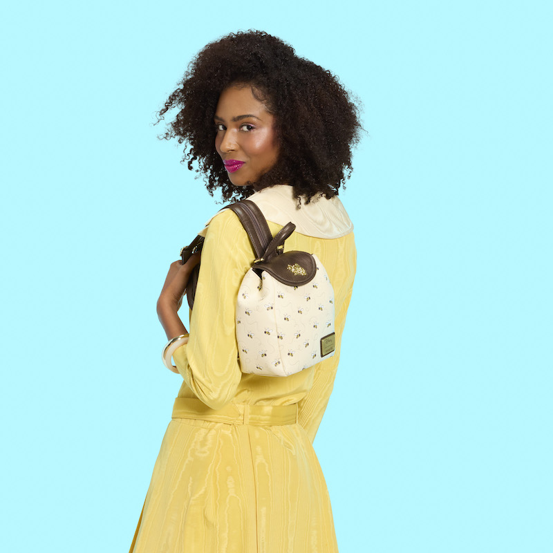 Woman wearing a yellow dress, facing away from camera, and looking over her shoulder at the camera. She wears the Loungefly Winnie the Pooh micro mini backpack over a shoulder. 
