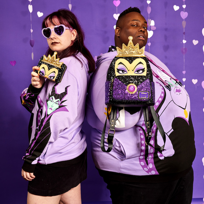 Woman and man standing back to bag wearing the Loungefly Curse Your Hearts Hoodie and holding the Loungefly Snow White Evil Queen Exclusive Sequin Cosplay Mini Backpack and Wallet 