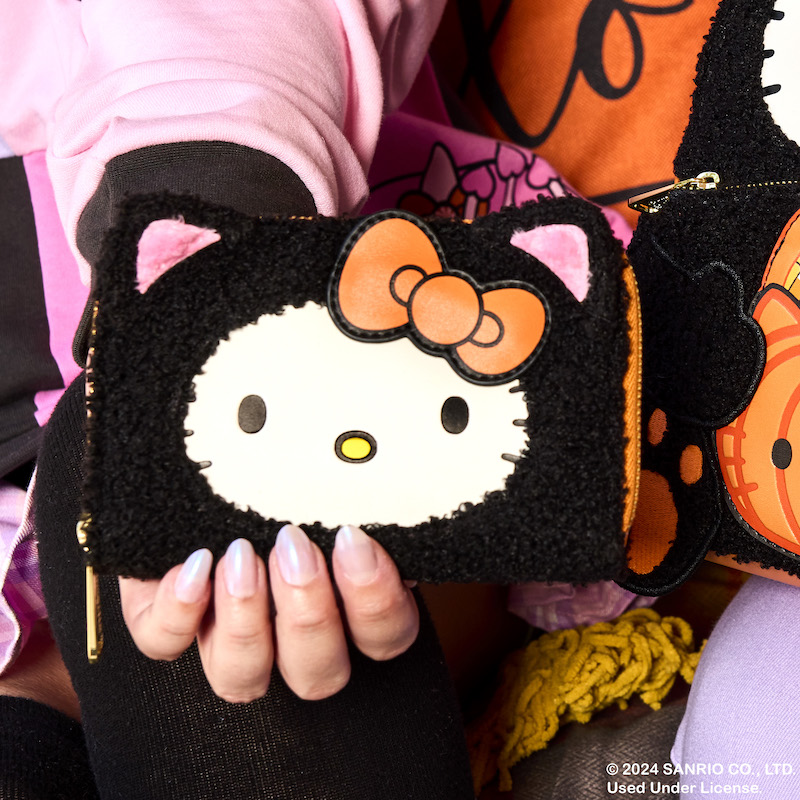 Woman holding the sherpa Hello Kitty Costume wallet toward camera, featuring Hello Kitty dressed as a black cat for Halloween.