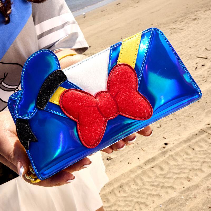 Person standing on the beach, holding the shining, metallic exclusive Loungefly Donald Duck 90th Anniversary wallet to the camera