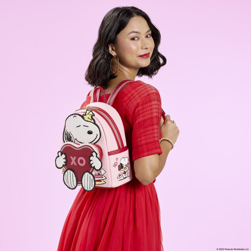 The Loungefly Peanuts Snoopy Valentine&rsquo;s Day mini backpack and charm crossbody bag sit together on a pink background. 