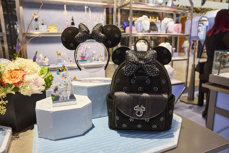 Loungefly Minnie Mouse mini backpack and ear headband with Swarovski crystals on display next to a Disney Swarovski figurine