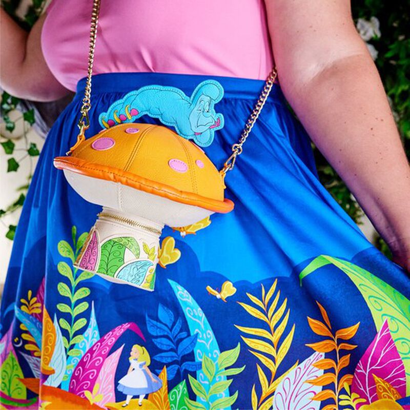 Woman wearing a pink top and a blue Alice in Wonderland skirt with the Stitch Shoppe Alice in Wonderland Figural Caterpillar Mushroom Crossbody Bag