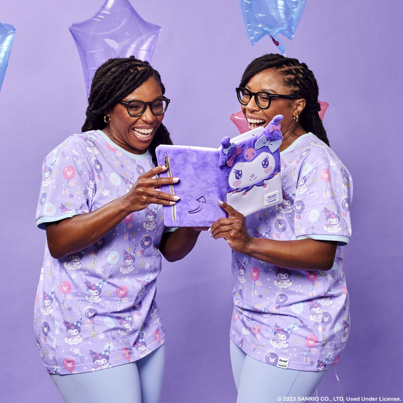 Twin women holding the Kuromi Plush Journal between the two of them and laughing together. They stand against a purple background with star-shaped balloons. 