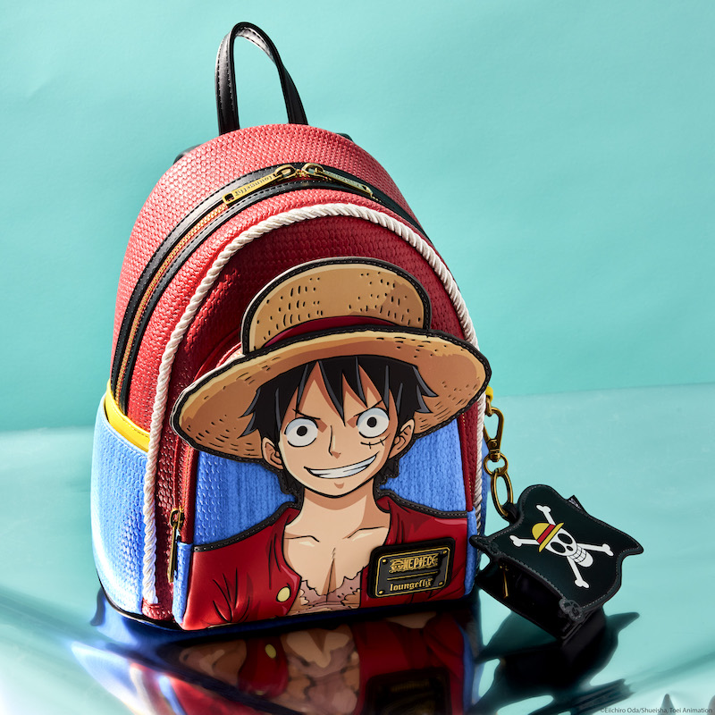 Loungefly One Piece mini backpack featuring Luffy on the front of the red and blue bag. It sits against a light blue background that looks like an open sea. Beside the bag sits the coin bag that looks like the pirate flag. 