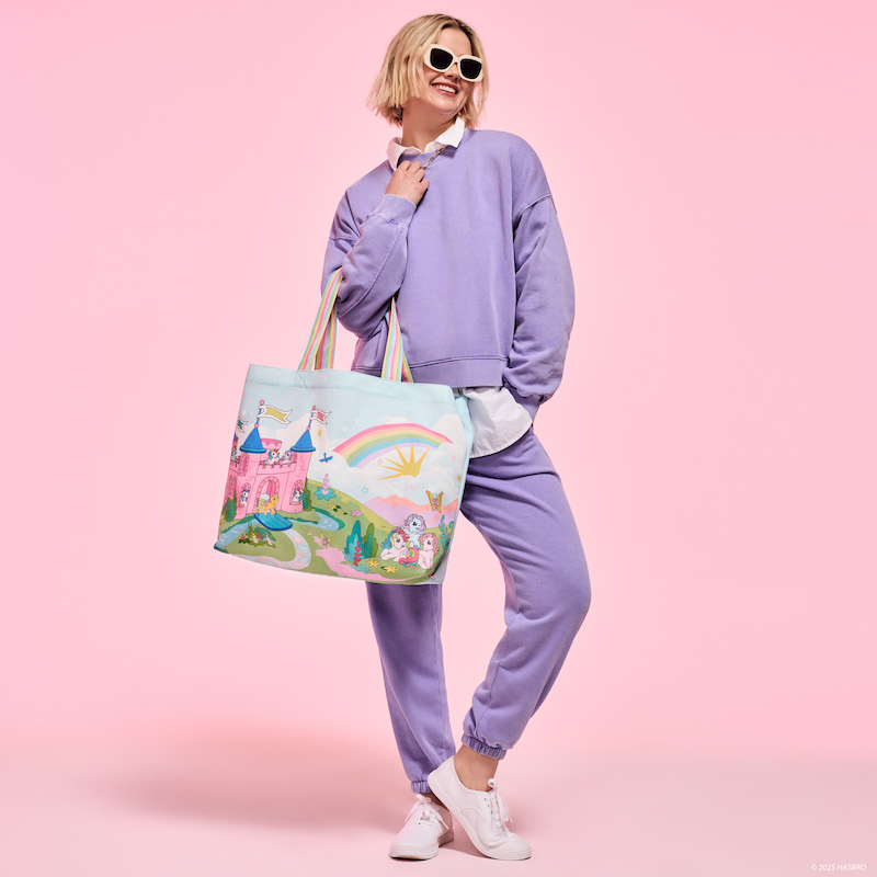 Woman wearing a purple sweatsuit ensemble and sunglasses, carrying the Loungefly My Little Pony Tote Bag. She stands against a pink background. 