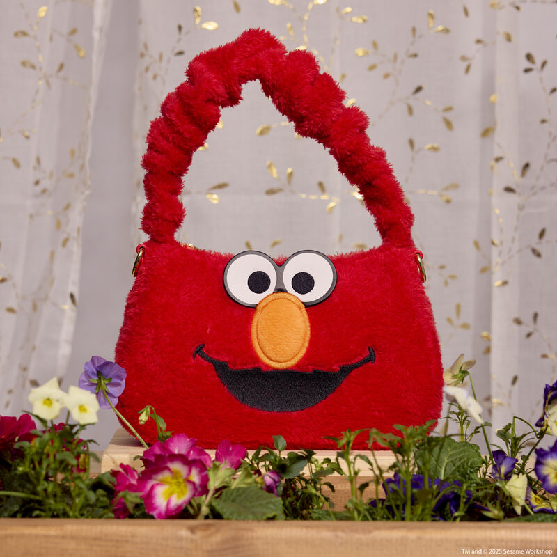 Red plush Loungefly Elmo crossbody bag with embroidered and applique details and a scrunchie-like handle sitting on a windowsill with a flowerbed. White translucent curtains sit behind the bag. 