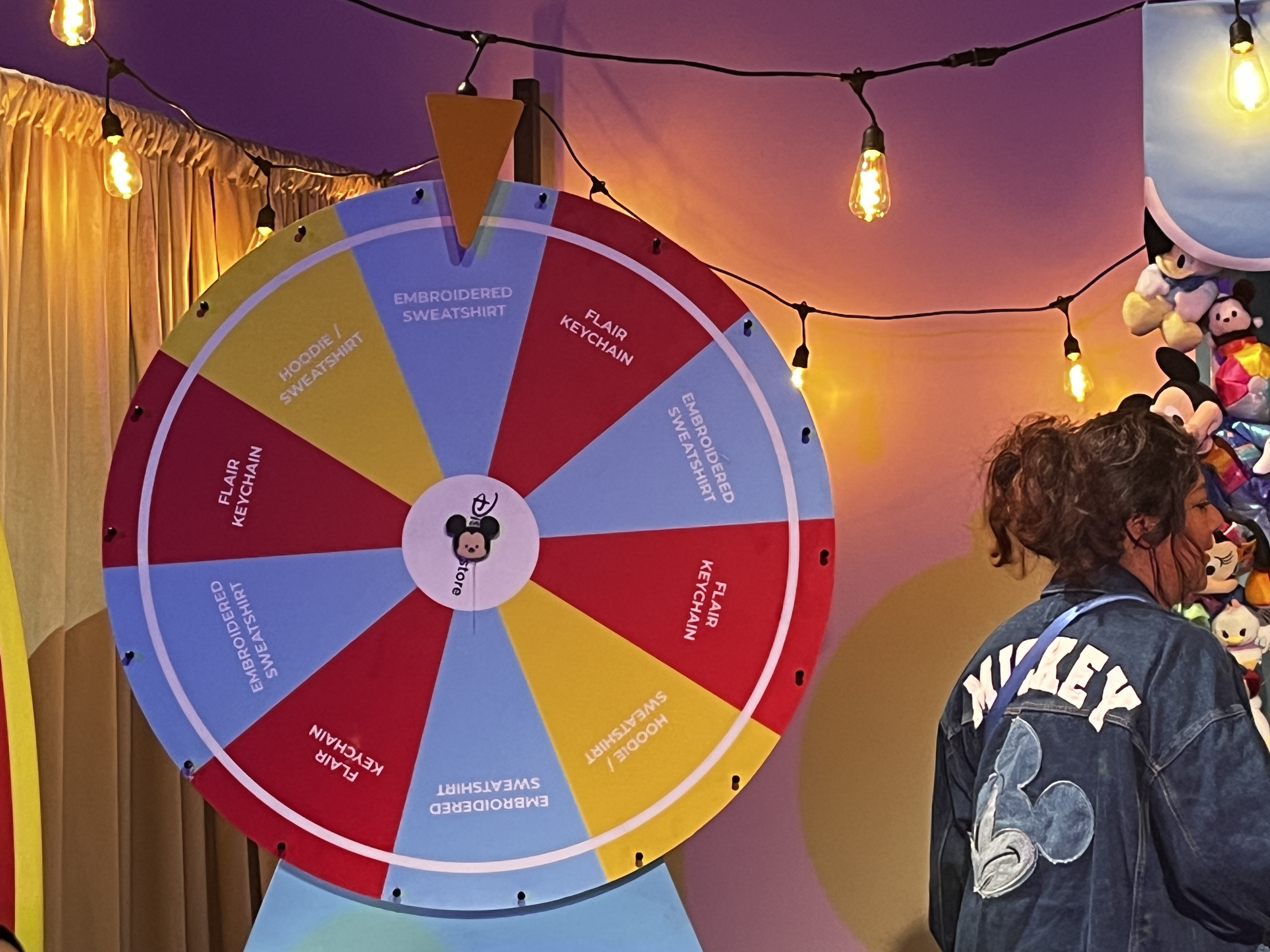 Image of a Disney prize wheel with prizes such as "embroidered sweater" "sweatshirt/hoodie" and "flair keychain"