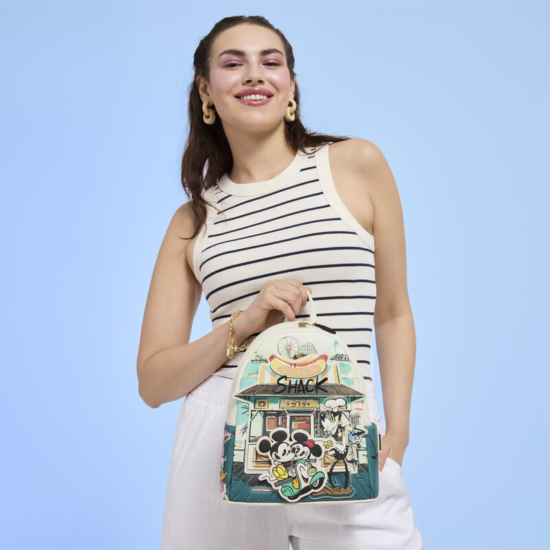 Woman wearing a black and white striped shirt and holding the Loungefly Mickey and Friends Snack Shack mini backpack.