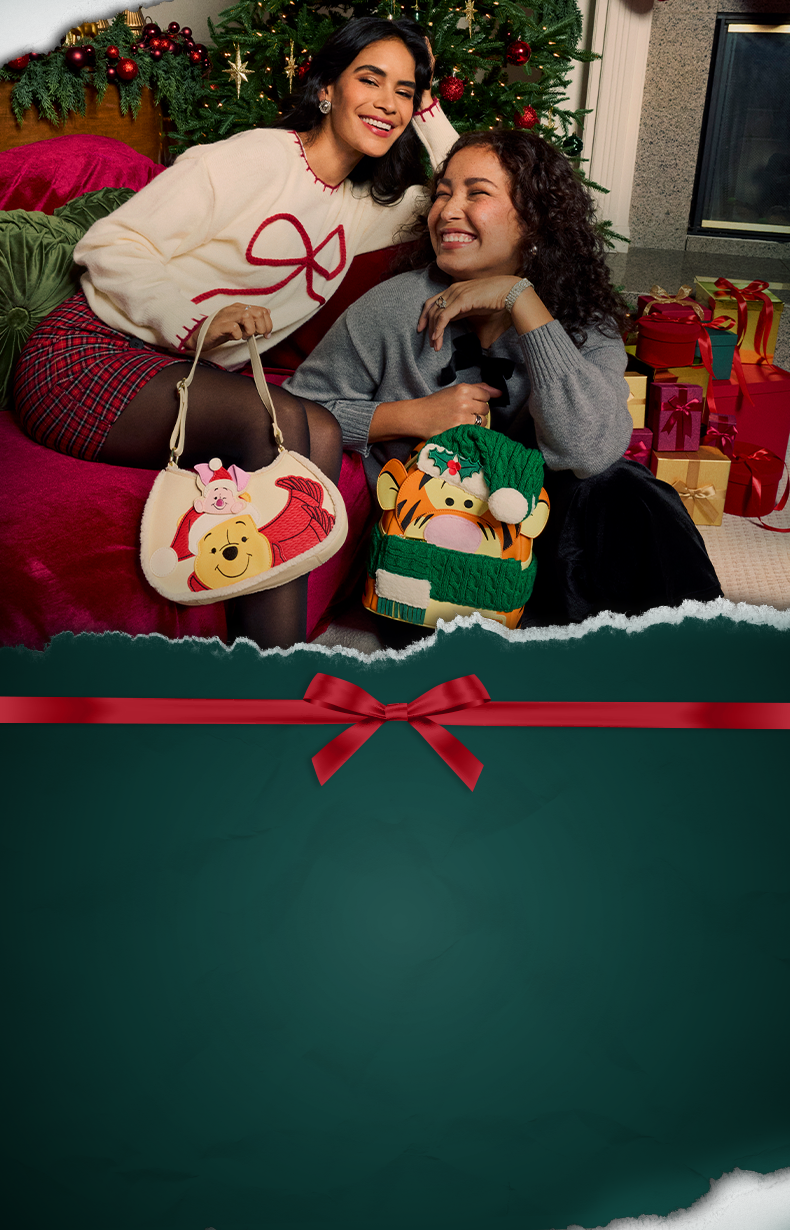 Two women celebrating Christmas with Disney Winnie the Pooh and Tigger Loungefly bags beside a decorated tree and gifts
