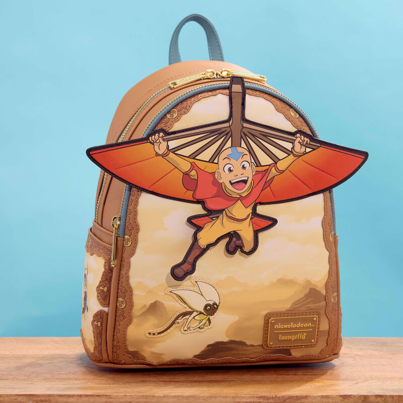 Loungefly Avatar: The Last Airbender mini backpack featuring Aang flying with his glider in applique detail. The bag sits on a wooden table against a blue background. 