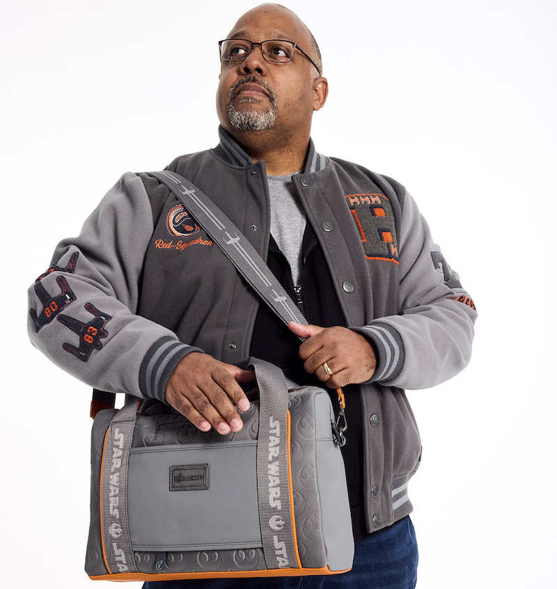 Man wearing the Loungefly COLLECTIV Star Wars Rebel Alliance The EXECUTIV Laptop Bag and looking away from camera, standing against a white background. The EXECUTIV laptop bag is grey and has subtle Star Wars symbols on it with orange highlights. 
