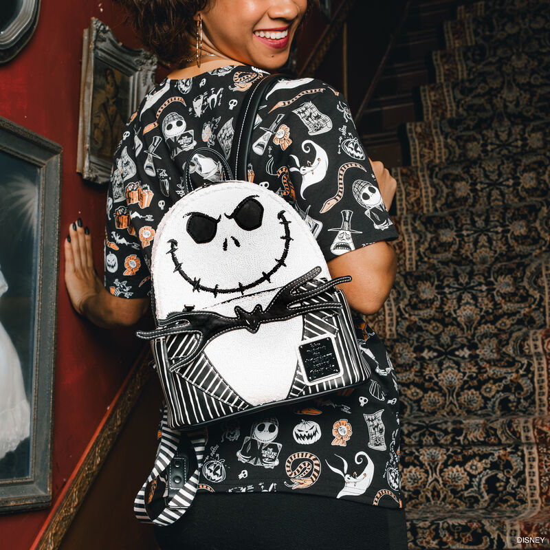 Woman facing away from camera looking over her shoulder and smiling, wearing a Loungefly Nightmare Before Christmas tee and wearing the Loungefly sequin Jack Skellington mini backpack. 