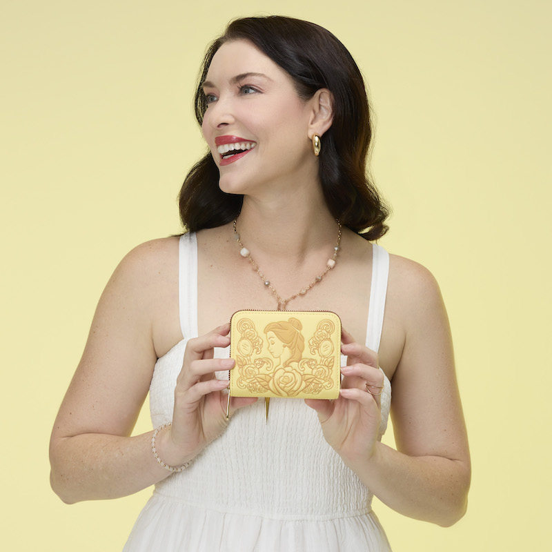 Woman wearing a white dress, smiling, holding the Loungefly Disney Beauty and the Beast Princess Belle Zip Around Wallet. 