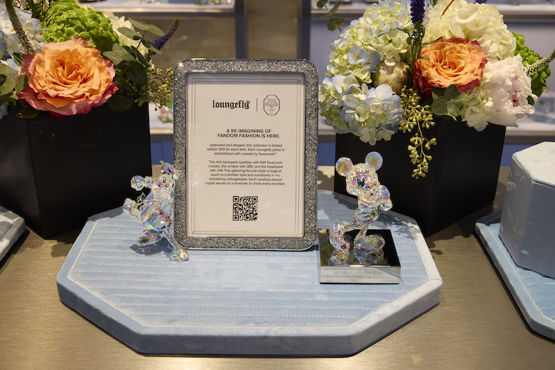 Close up of the Loungefly Disney Swarovski product display, showcasing a display that describes the collection, flanked by two Disney Swarovski figurines 