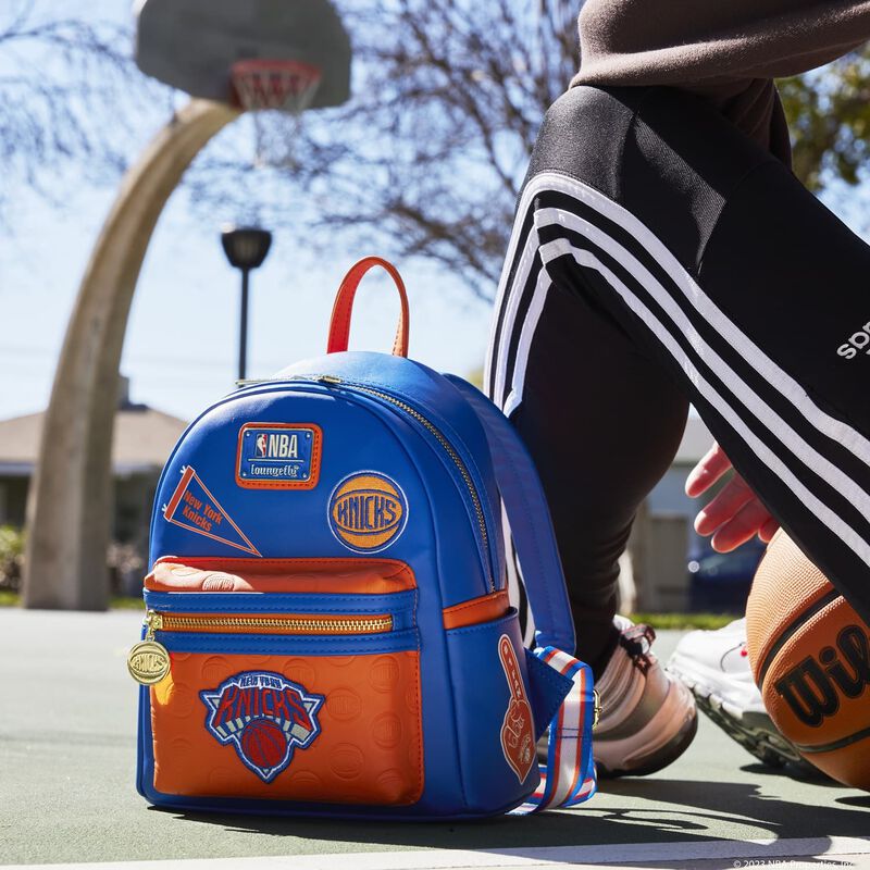 Image of our Knicks Patch Icons Mini Backpack outside on a basketball court next to someone sitting down 