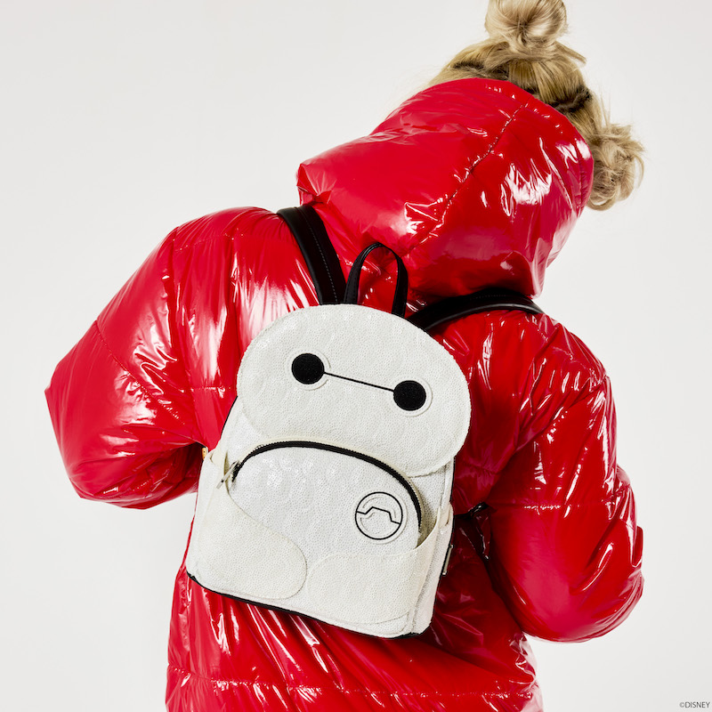 Woman wearing a shiny red hoodie, facing away from camera wearing the Loungefly Disney Big Hero 6 10th Anniversary Baymax Mini Backpack, featuring glow-in-the-dark sequins.