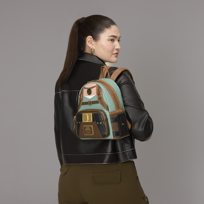 Woman facing away from camera, wearing olive pants and a black leather jacket. She wears the Loungefly Tomb Raider Lara Croft mini backpack over a shoulder. 