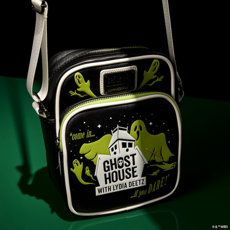 Loungefly Beetlejuice Beetlejuice Ghost House Glow Crossbody Bag sitting half in shadow against a green background.