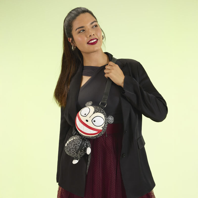 Woman wearing the Vampire Teddy Figural bag crossbody, wearing a black and maroon ensemble. She stands against a soft yellow/green background. 