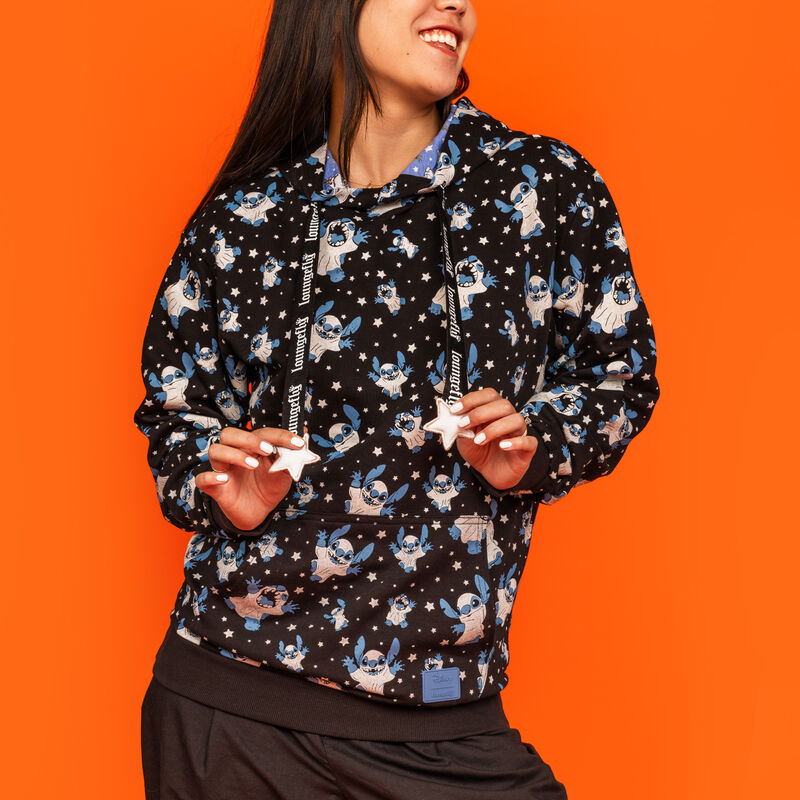 Woman standing against an orange background wearing the Loungefly Stitch Ghost Costume All-Over Print Unisex Hoodie, featuring Stitch dressed as a ghost all over the hoodie. 