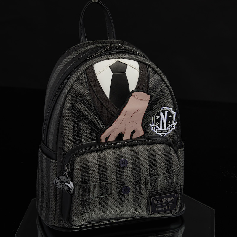 Black and gray Loungefly mini backpack that looks like Wednesday Addams' striped Nevermore Academy uniform. Thing pops up in appliqué detail behind the front pocket. The bag sits against a black background. 