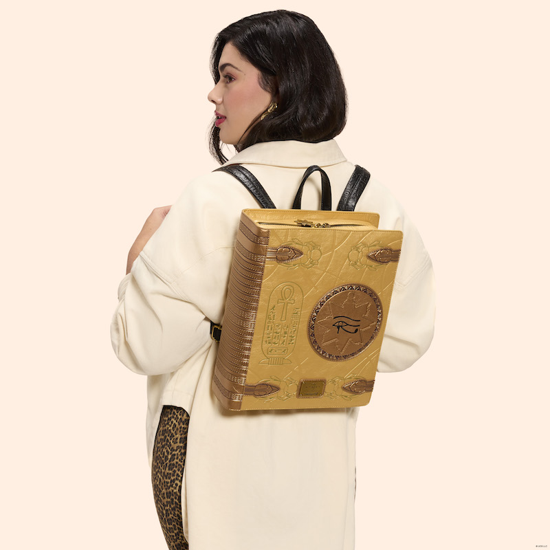 Woman facing away from camera, wearing cheetah-print pants and a long white sweater/coat. She wears the Loungefly The Mummy Book of the Living bag on her back. 