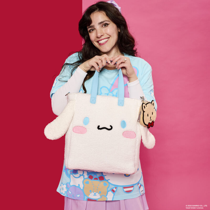 Woman smiling at camera and holding up the Loungefly Sanrio Cinnamoroll Cosplay Sherpa Tote Bag with Coin Bag. The tote bag features Cinnamoroll with 3D ears sticking out from the sides, and the bag is covered in white sherpa material.