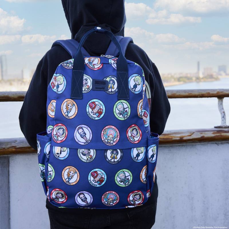Person in a hoodie facing away from camera, standing on a dock looking out on the water, wearing the Loungefly One Piece full-size nylon backpack, which features an all over print of various One Piece characters framed in circles. Characters featured include Luffy, Usopp, Robin, Zoro, Franky, Chopper, Sanji, Nami, and Brook. 