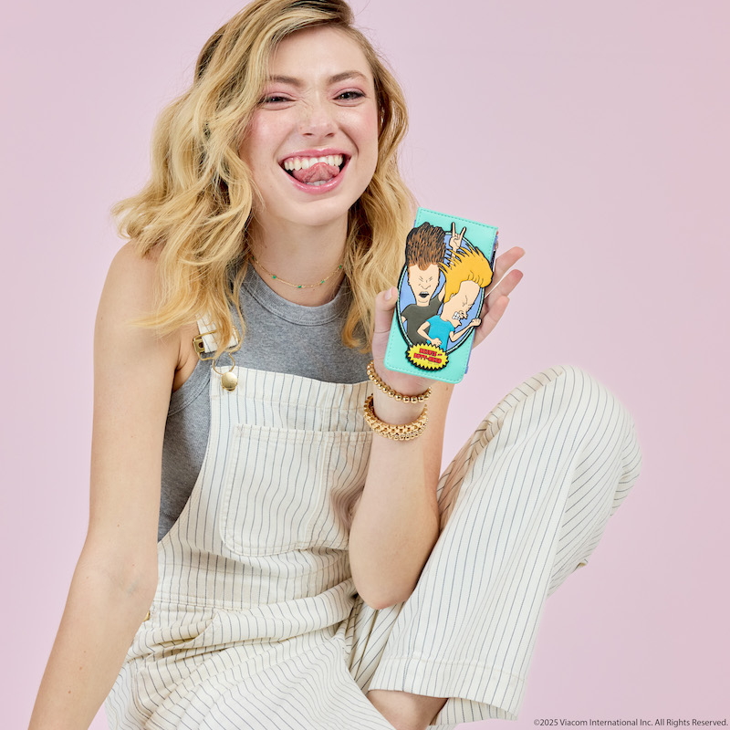 Woman sitting in front of camera with one knee up and holding up the Loungefly Exclusive Beavis and Butt-Head card holder. She sits against a light pink background. 
