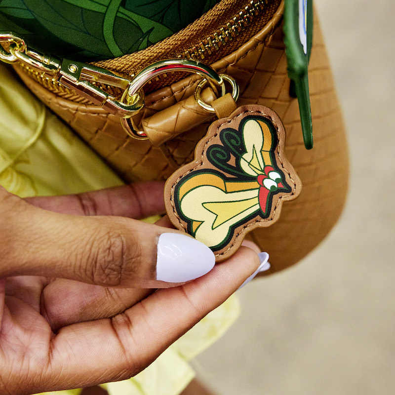 Close up image of the Alice in Wonderland Flowers Crossbody with someone holding the "bread and butterfly" charm 