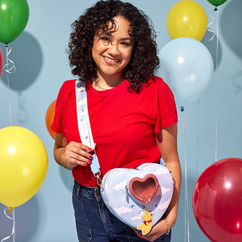 Image of woman wearing a red shirt and surrounded by balloons wearing the Loungefly Disney Winnie the Pooh & Friends Floating Balloons Heart Figural Crossbody Bag 
