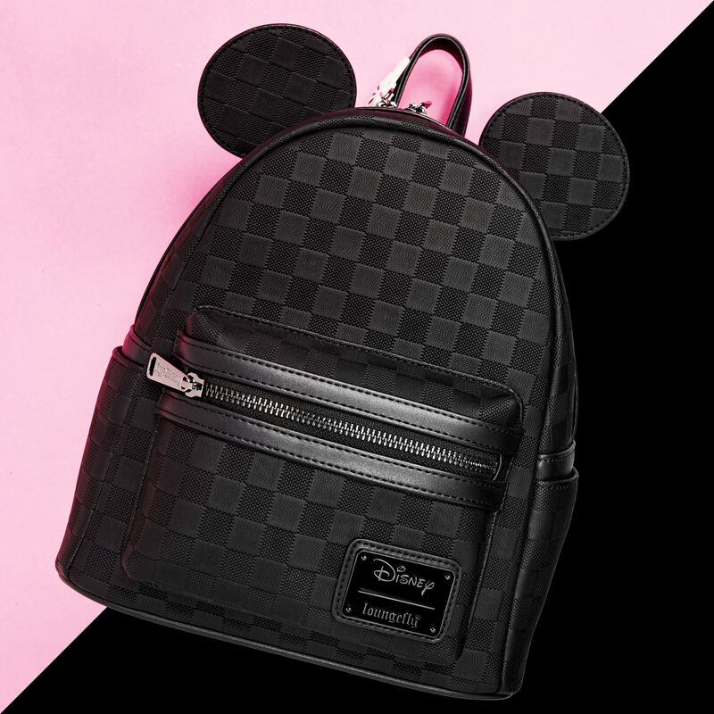 All black Loungefly Mickey Mouse mini backpack with a textured checkerboard pattern on it. The bag sits against a pink and black background.