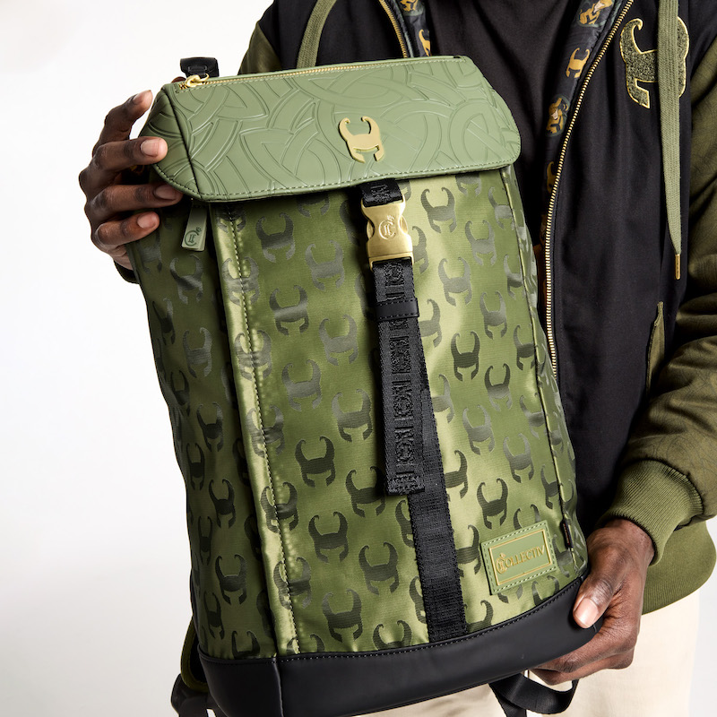 Man holding the Loungefly COLLECTIV Marvel Loki The TRAVELR Full Size Backpack, which features a repeating pattern of Loki's helmet all over the green backpack with a gold metal rivet of Loki's helmet on the top flap. 