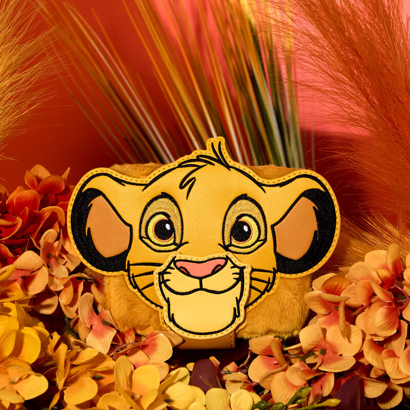 Plush Simba wallet featuring an appliqué of Simba smiling. The wallet sits on a bed of orange flowers against a pink-orange background