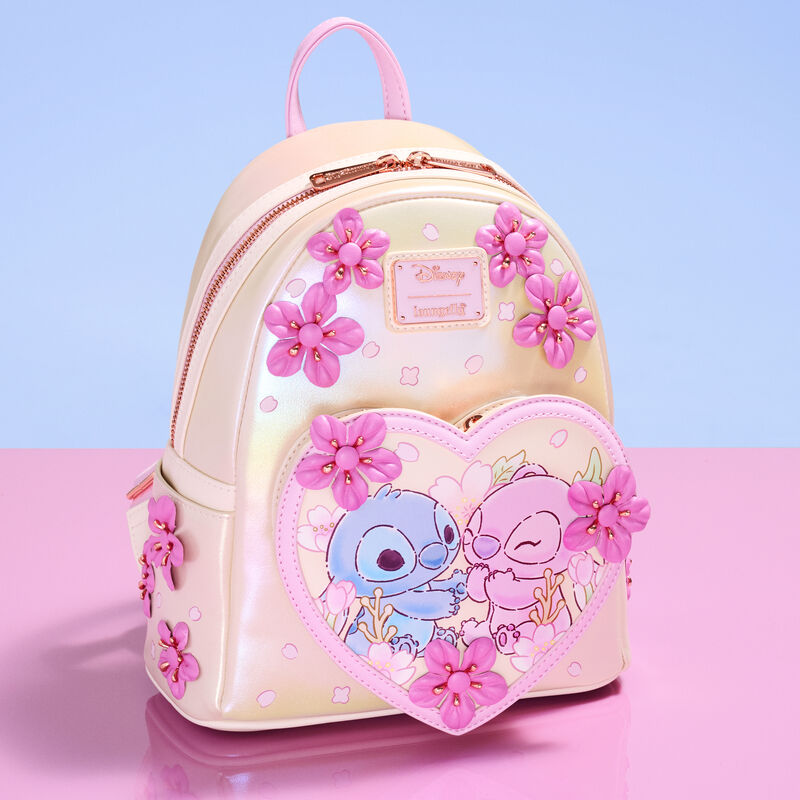 Loungefly mini backpack featuring 3D cherry blossoms and Stitch and Angel sitting together in a heart-shaped front pocket. The bag sits against a pink and purple background.