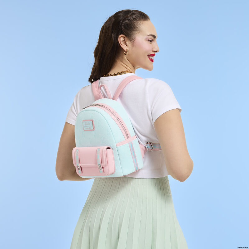 Woman facing away from camera wearing a white top and green skirt. She wears the pink and blue Loungefly Classic Barbie Terry Cloth mini backpack. She stands against a light blue background. 