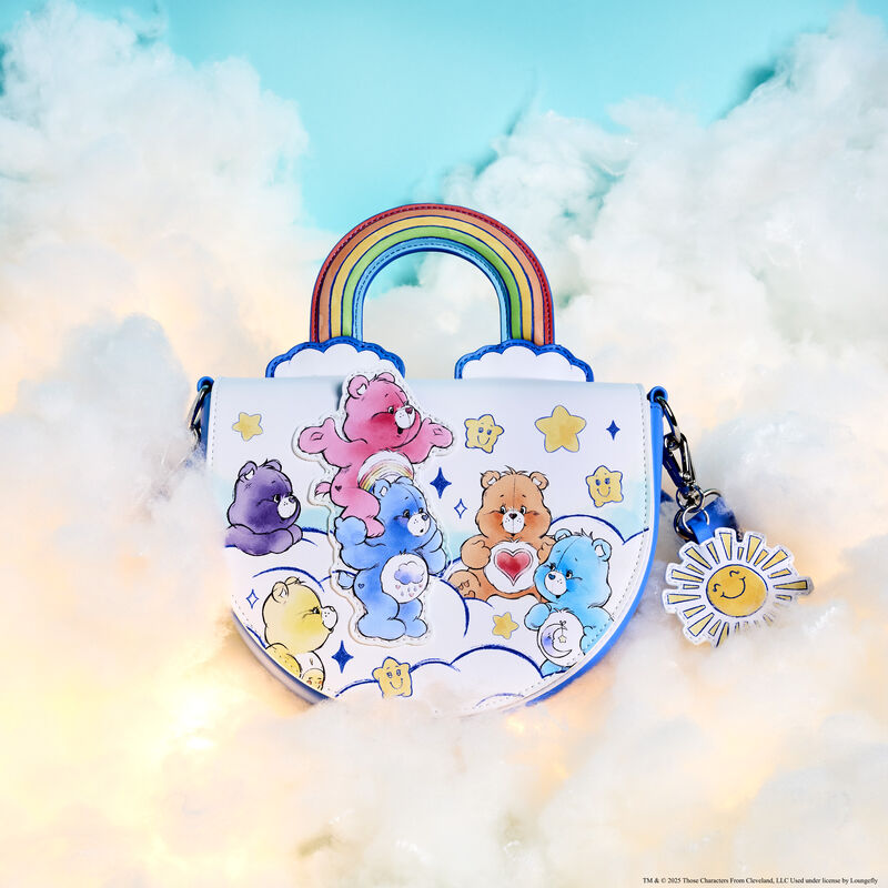 Loungefly Care Bears Care-A-Lot Rainbow Handle Crossbody Bag featuring several Care Bears on white clouds surrounded by smiling stars and sparkles. The handle of the crossbody bag is in the shape of a rainbow. The bag sits on fluffy white clouds against a blue background.