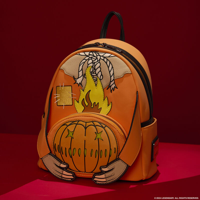 Loungefly Trick 'r Treat mini backpack featuring Sam's outfit with 3D arms that hold a jack-o'-lantern on the front pocket. The bag sits against a red background. 