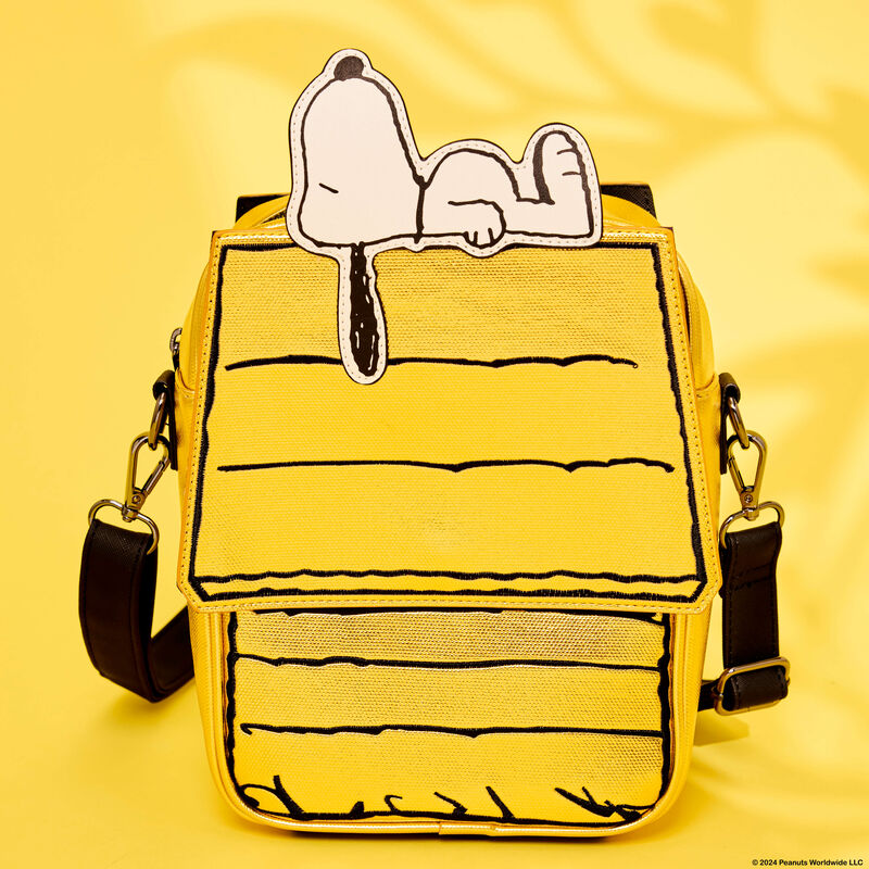 Yellow figural Loungefly crossbody bag in the form of Snoopy's doghouse with an appliqué of Snoopy sleeping on the top of it. The bag sits against a yellow background. 