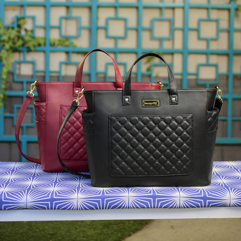 The red and black The Mo Convertible Backpack and Tote Bag sitting on a purple surface outside with a green fence behind them. 