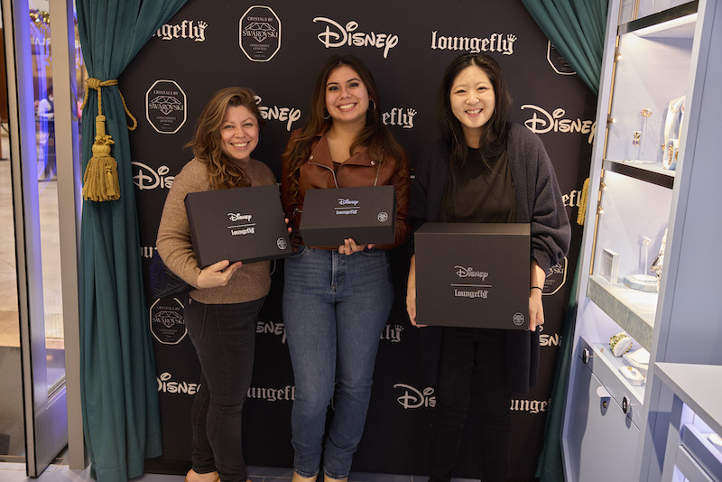 Three women standing together smiling holding black boxes that have their raffle prizes, pieces of the Loungefly Disney Swarovski collection!