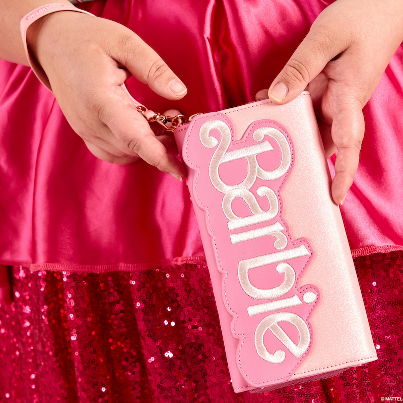 Close-up image of a woman holding the exclusive Loungefly Barbie 65th anniversary sequin wristlet wallet, which features the Barbie logo on the front flap of the wallet.