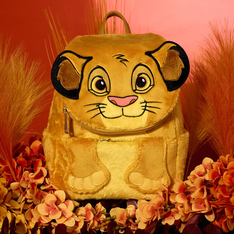 Plush Simba mini backpack sitting on a bed of orange flowers against a dark pink-orange background